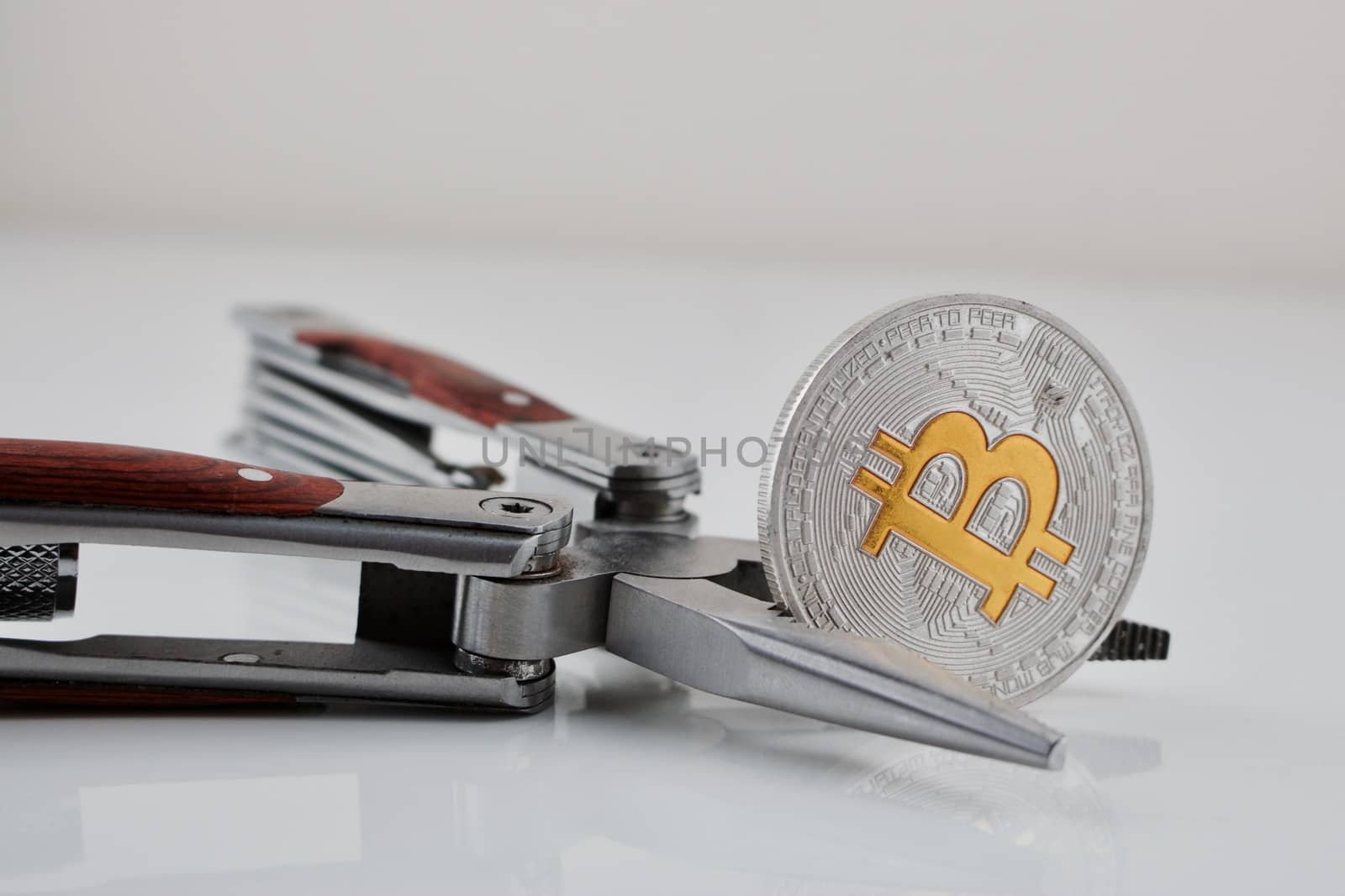 Digital currency physical silver bitcoin coin . Yellow sign "b" and pocket knife on the table.