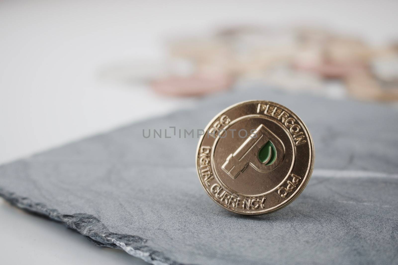 Digital currency physical gold peercoin coin with green leaf on the granite plate.