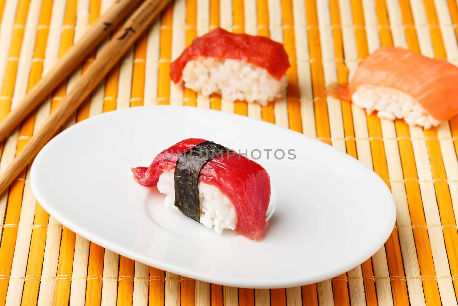  Red tuna Nigiri with Nori seaweed on white plate with chopsticks and other Nigiris. Raw fish in traditional Japanese sushi style. Horizontal image.