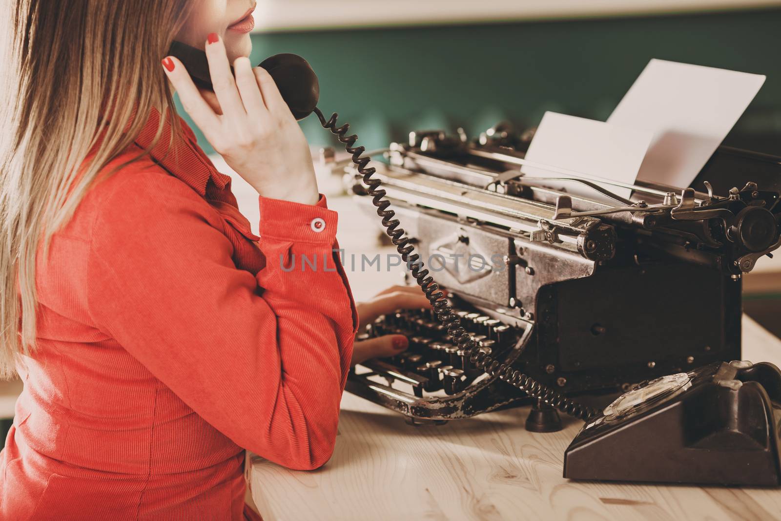 Secretary at old typewriter with telephone. Young woman using typewriter. Business concepts. Retro picture style.