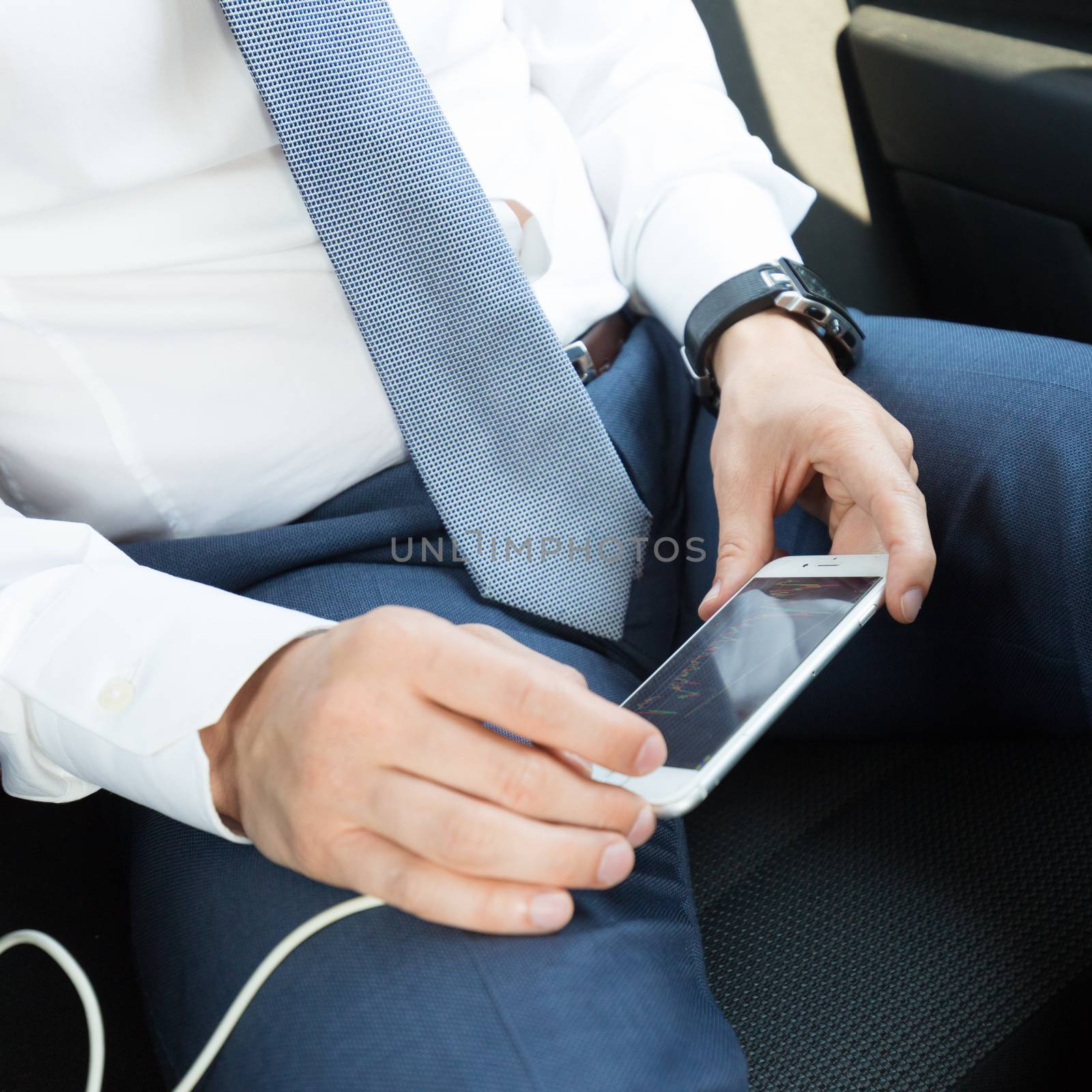 Close up of a businessman using smart phone while driving on the back seat of a car. Focus on mobile device.