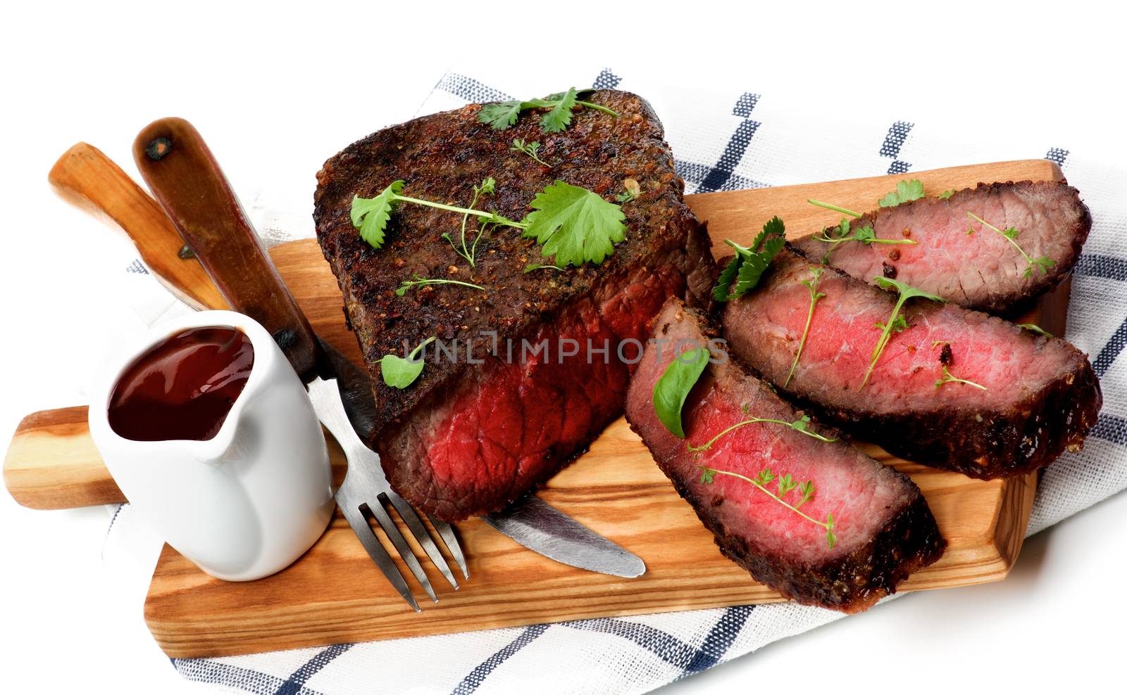 Sliced Delicious Roast Beef Medium Rare on Wooden Cutting Board with Tomato Sauce, Fork and Table Knife closeup on Checkered Napkin