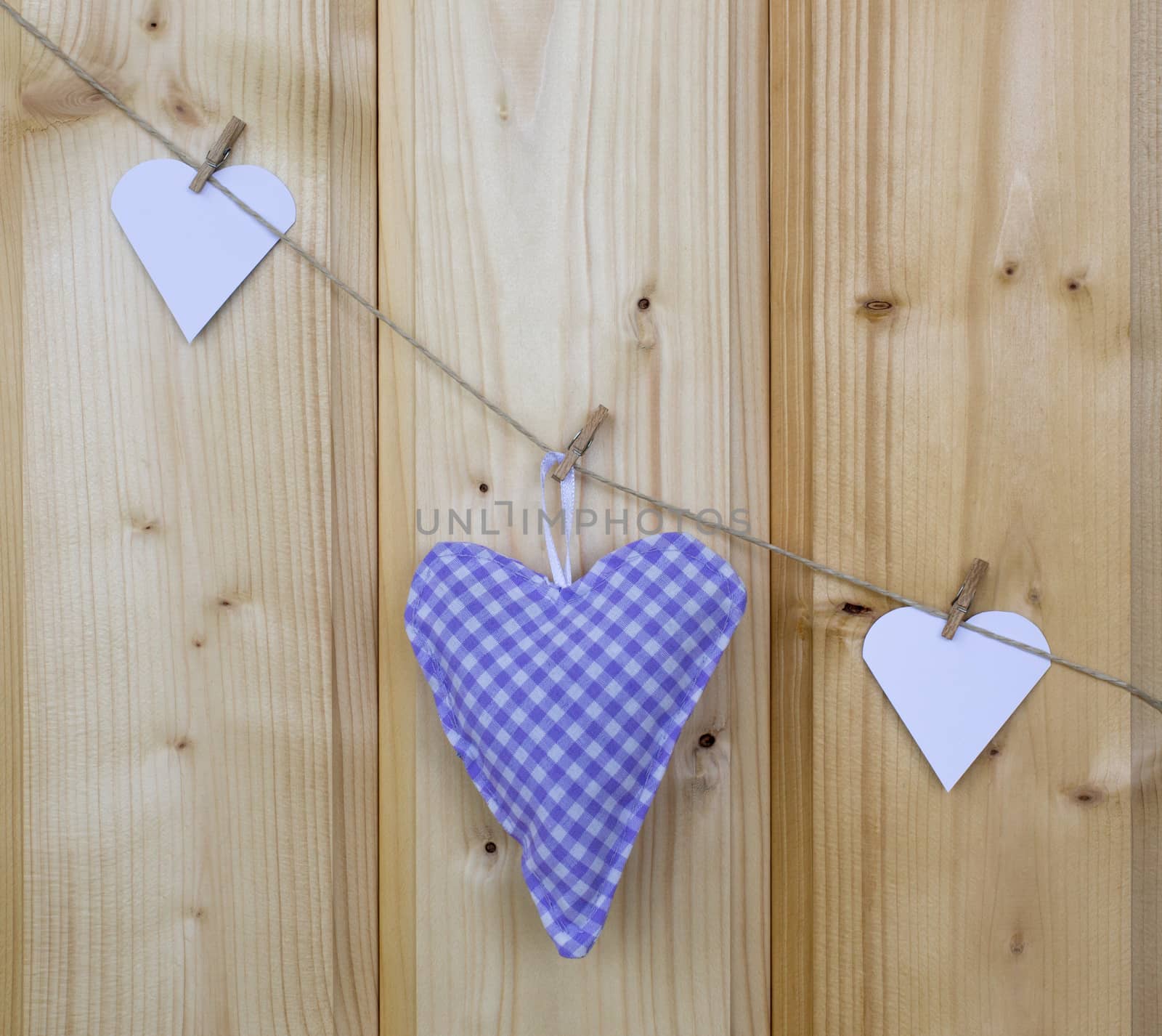 Three hearts with clothes pegs on a cord on wood