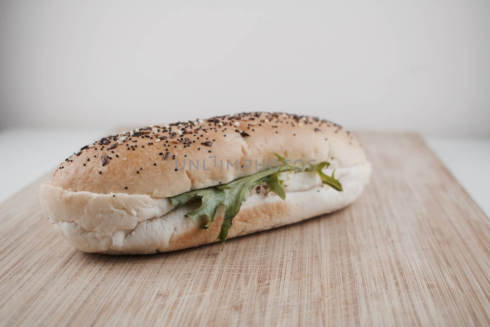 Fresh delicious roll with seeds, salad and tuna on wooden board in kitchen.