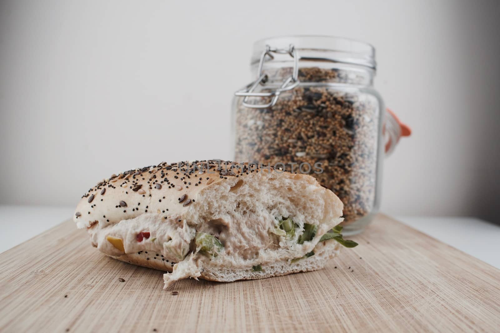 Tasty sandwich roll with a seeds, tuna, vegetables and salad near jar with seeds.