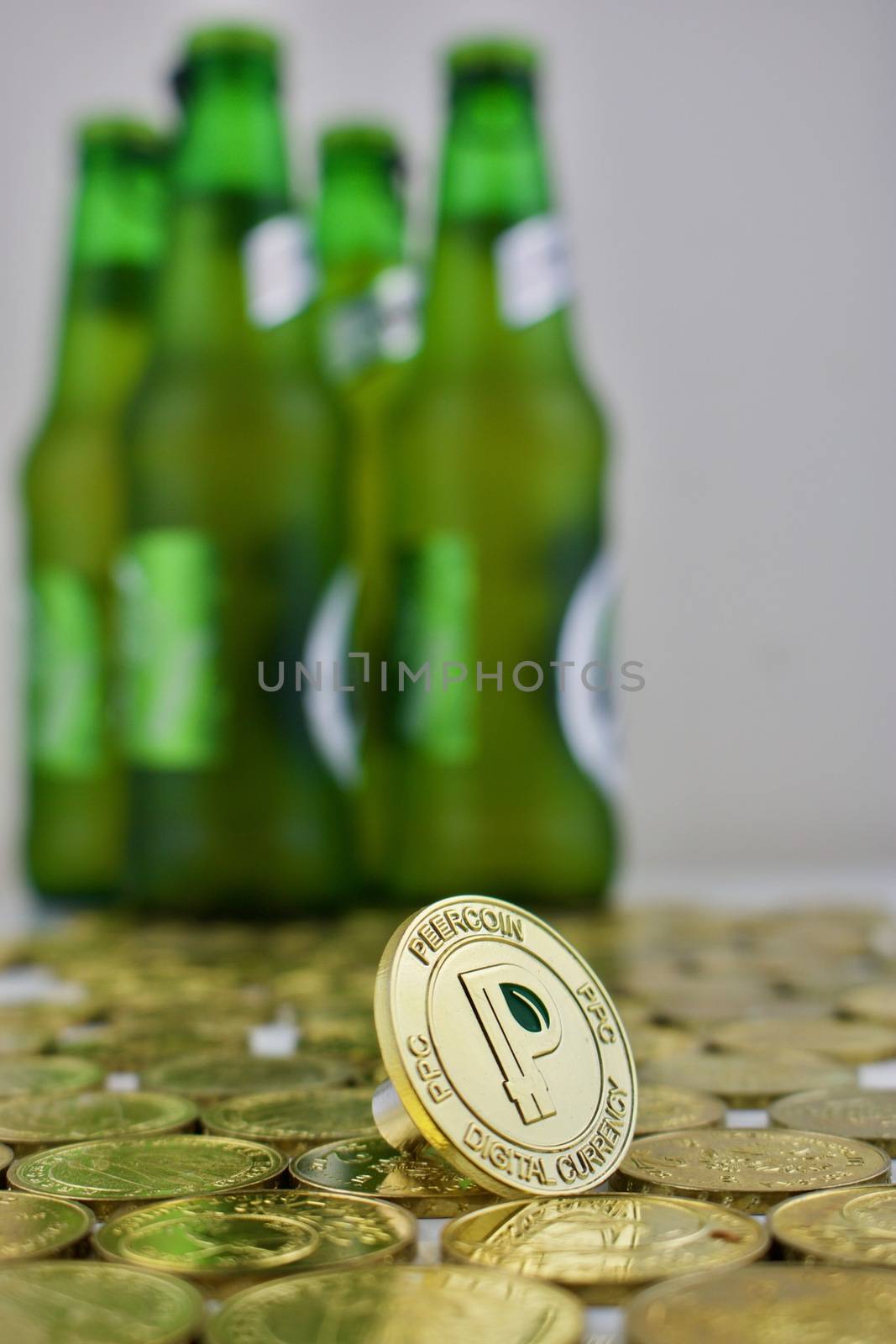 Digital currency physical gold peercoin coin with green leaf near green bottles.
