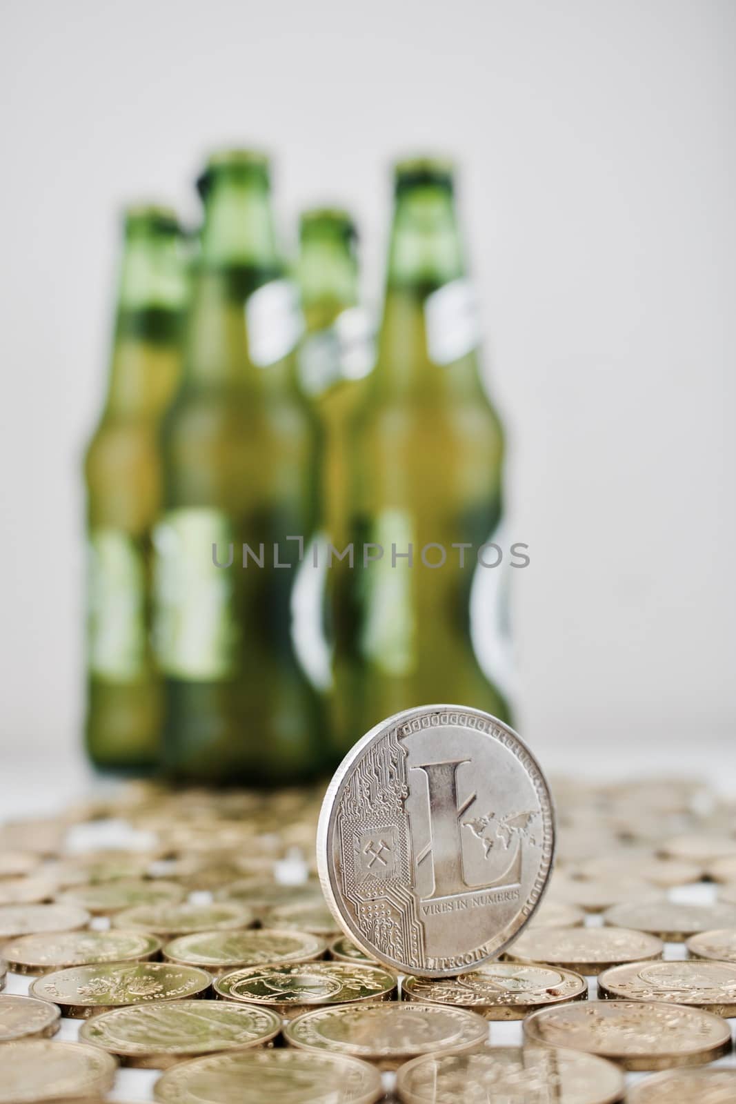 Digital currency physical silver litecoin coin on the money nerar green beer bottles.