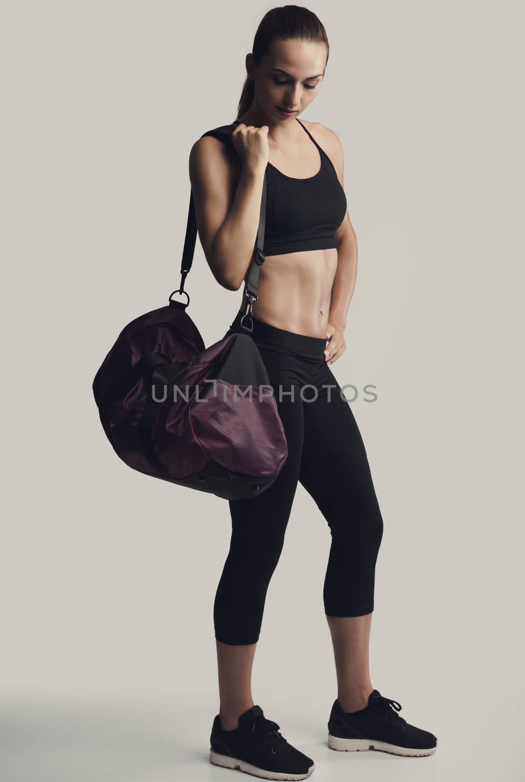 Portrait of sporty young woman posing with a gym bag,  against a gray background