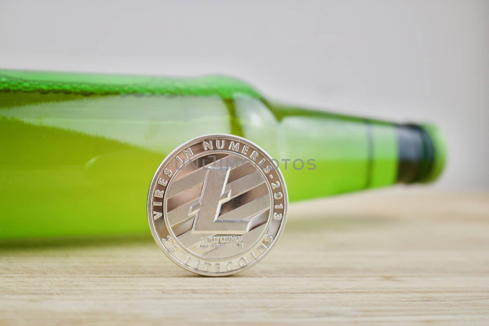 Digital currency silver Litecoin coin near green beer bottle. Drink concept.
