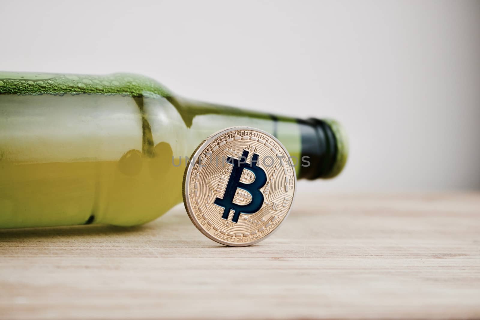Digital currency physical gold bitcoin coin on the wooden board near green beer glass bottle.