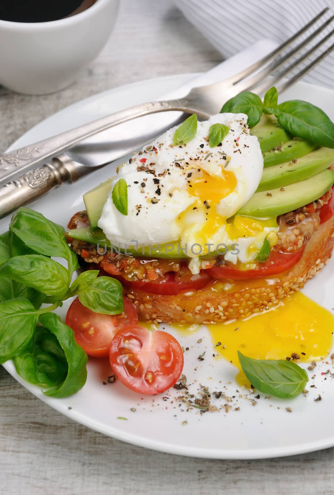 Egg poached on a toasted slice of baguette with tomato, spicy ham and avocado, sprinkled   spices and basil