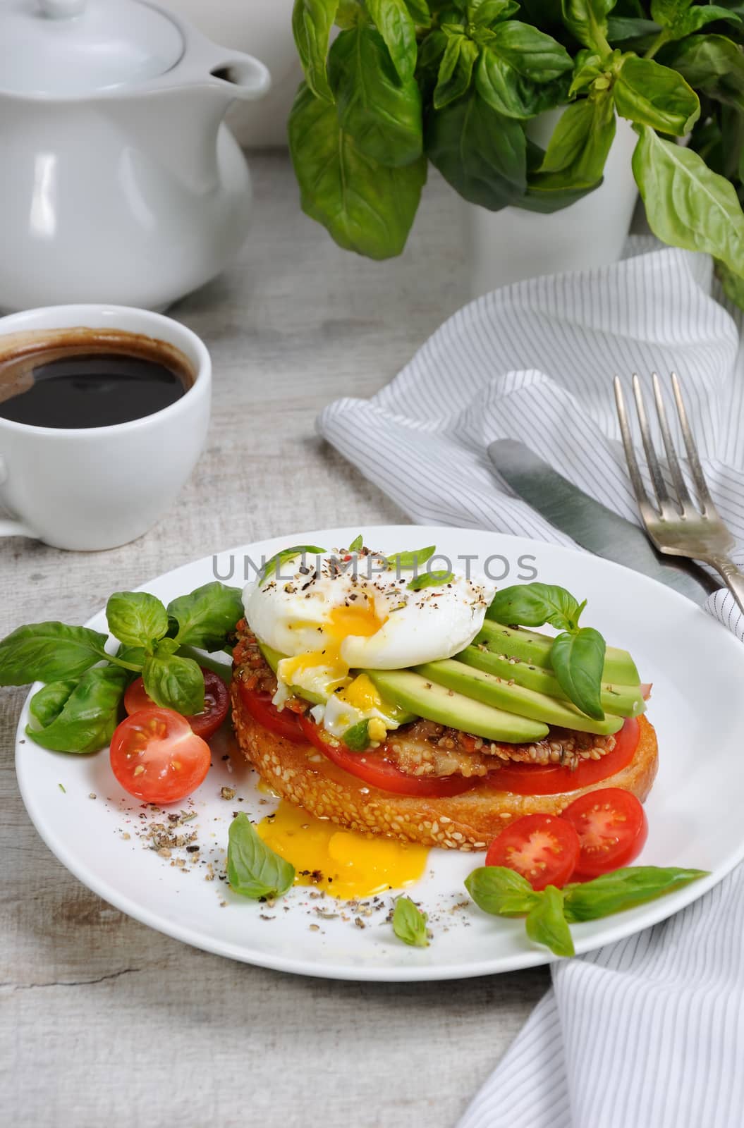 Egg poached on a toasted slice of baguette with tomato, spicy ham and avocado, sprinkled   spices and basil