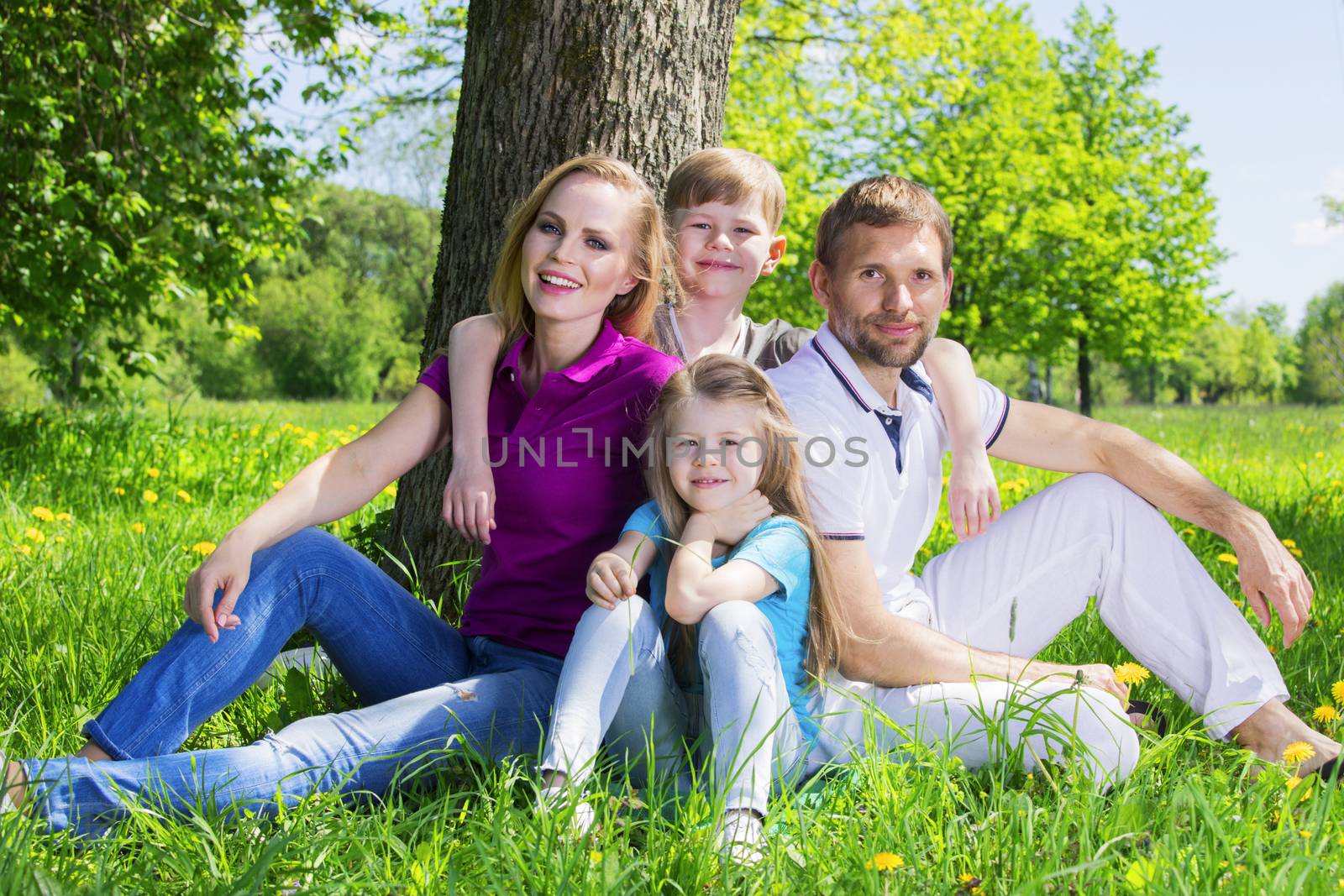 Father, mother and their children are sitting on the green grass in the summer park