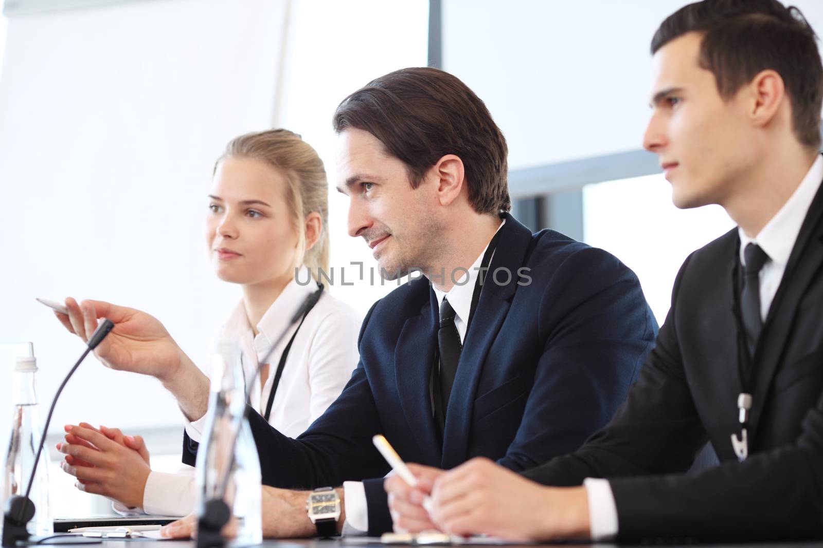 Group of speakers at business meeting at the table with microphones