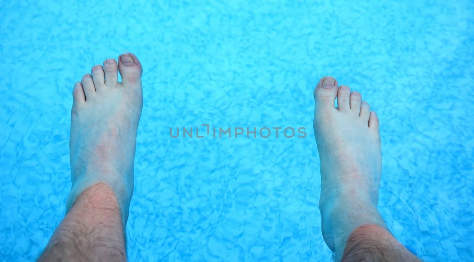 Top view on the feet refreshing in a clear water in the swimming pool.