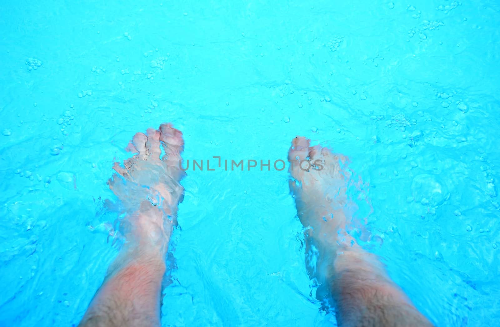 Top view on the feet refreshing in a clear water in the swimming pool.