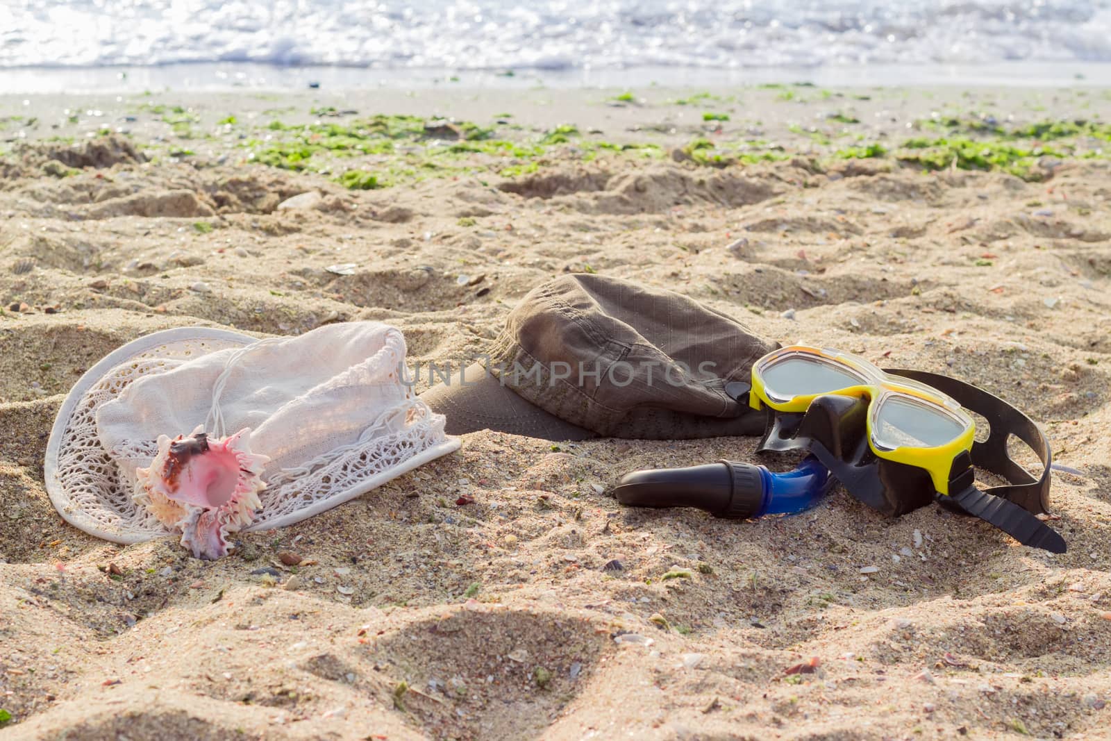 Women's hat for sun protection, men's cap and black and yellow diving mask with snorkel on the sandy beach against the sea at morning
