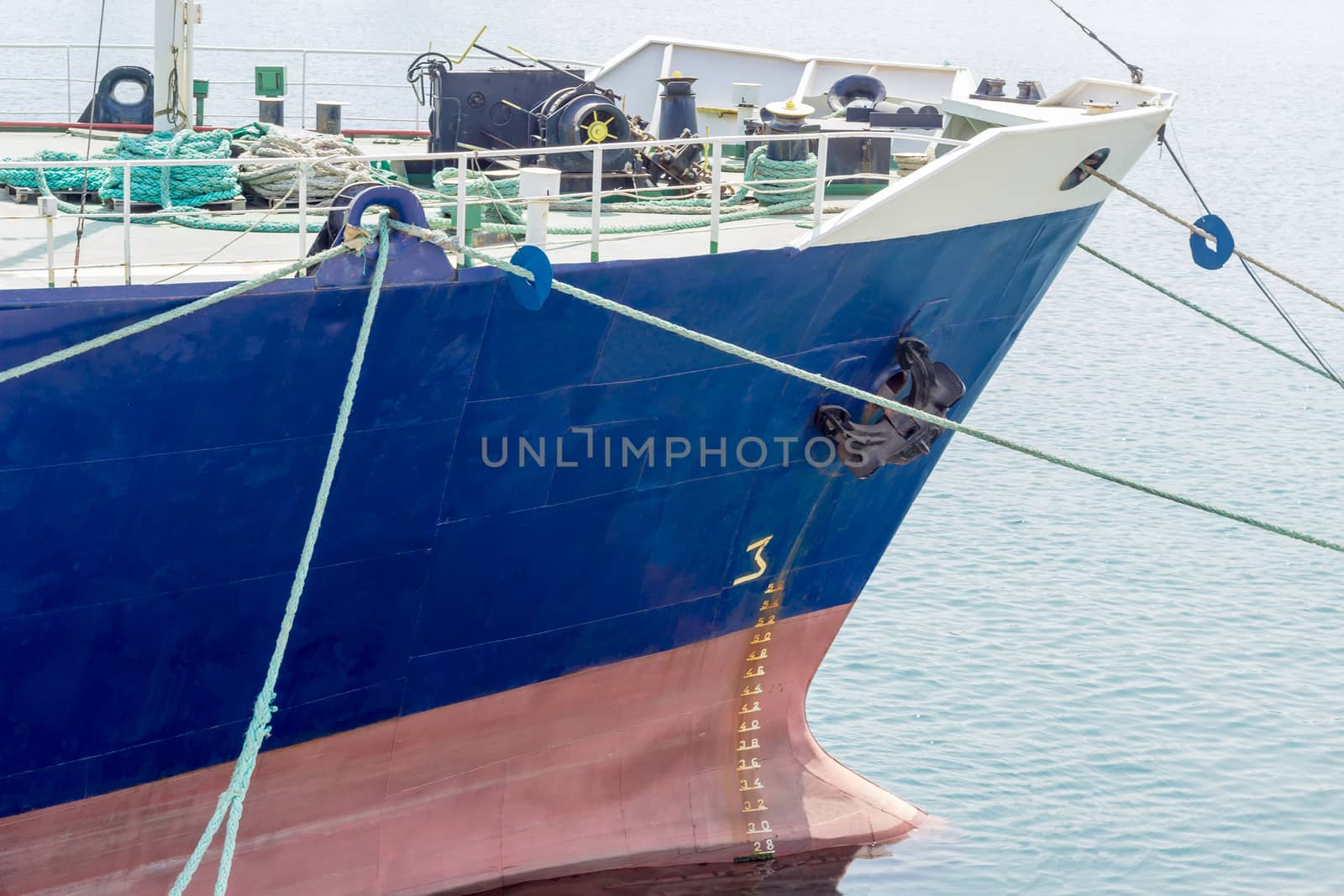 Bow of the old cargo ship with a blue starboard moored by several mooring ropes to the berth of the sea cargo port closeup
