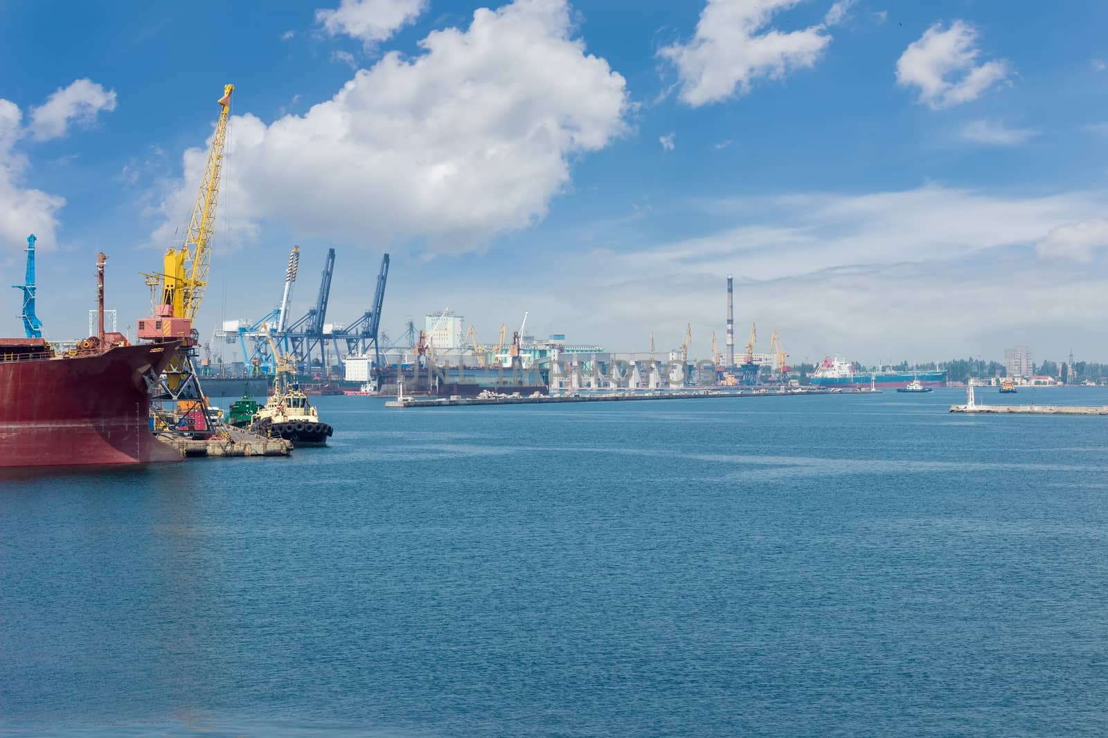 Part of the sea cargo port with several berth with different harbor cranes and bow of the ship in the foreground
