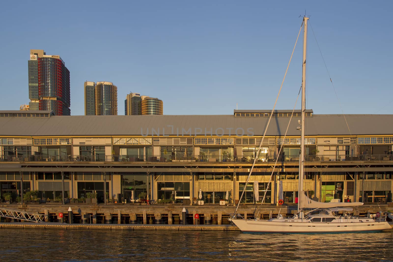 A sailboat infront of the historical Jones Bay Wharf office and restaurant building in Sydney Australia with the CBD skyscrapers in the background.