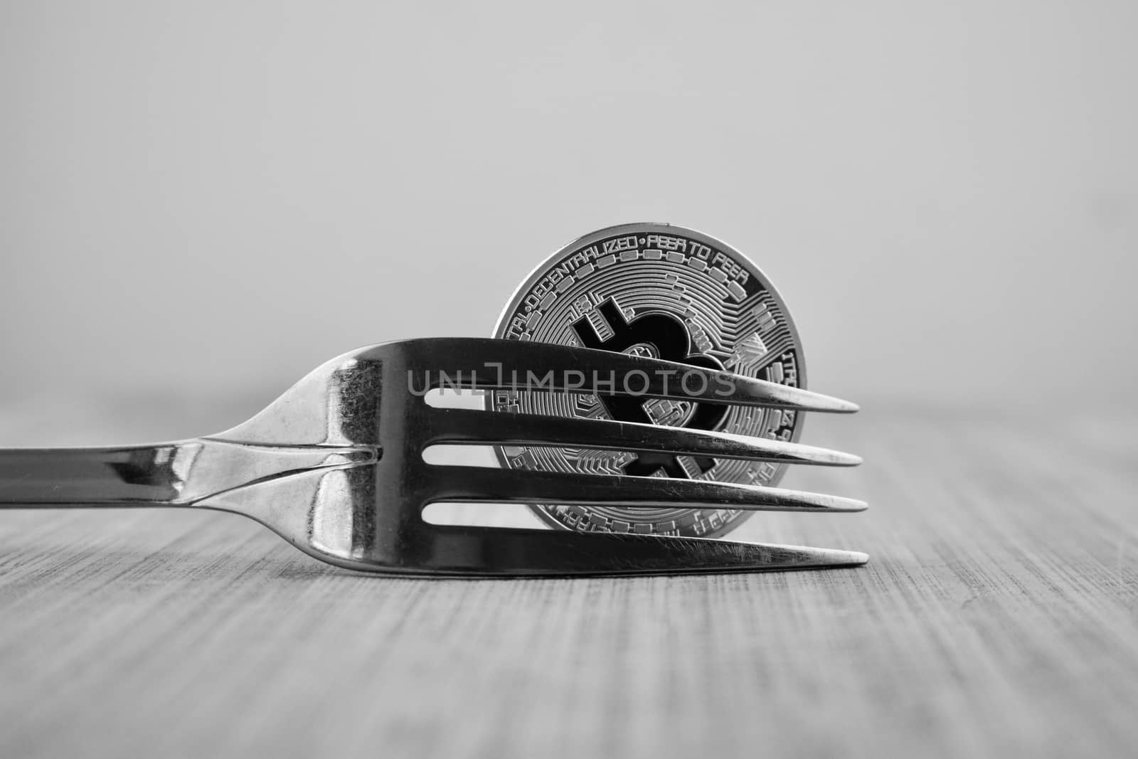Cryptocurrency physical silver bitcoin coin and fork on wooden board.
