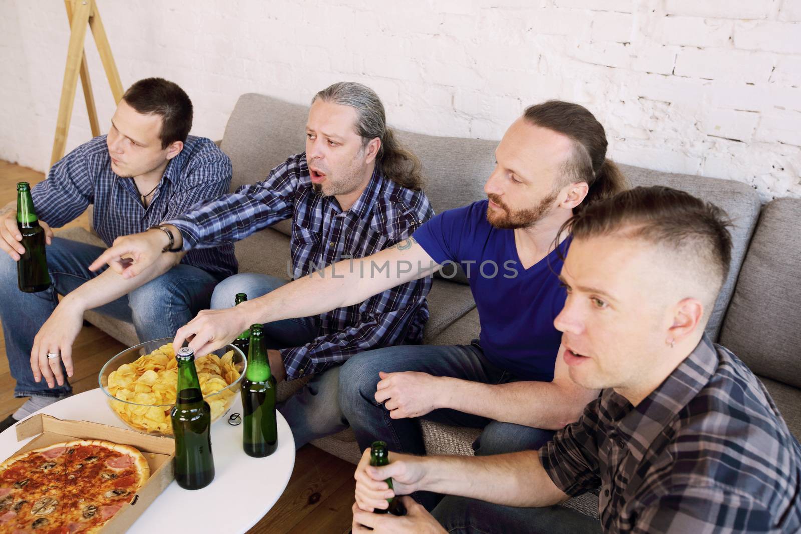 Male friends sports fans watching loosing football match on TV at home on couch sharing snacks drinking beer