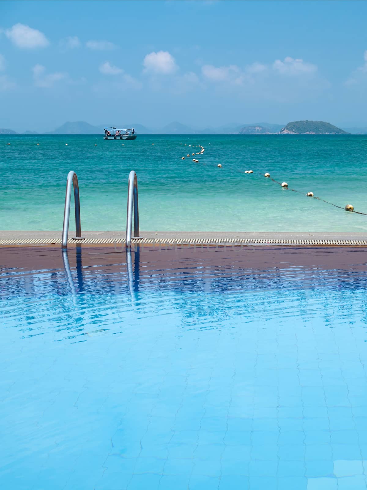 Outdoor swimming pool with emerald sea and boat