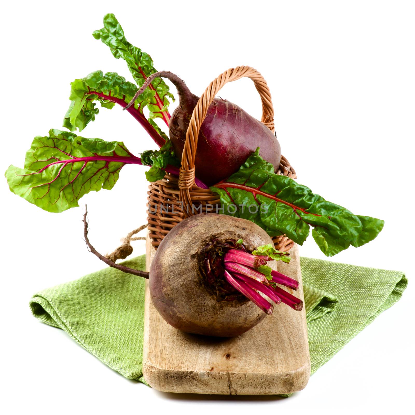 Two Fresh Raw Organic Beet Roots with Green Beet Tops in Wicker Basket on Wooden Board and Napkin isolated on White background