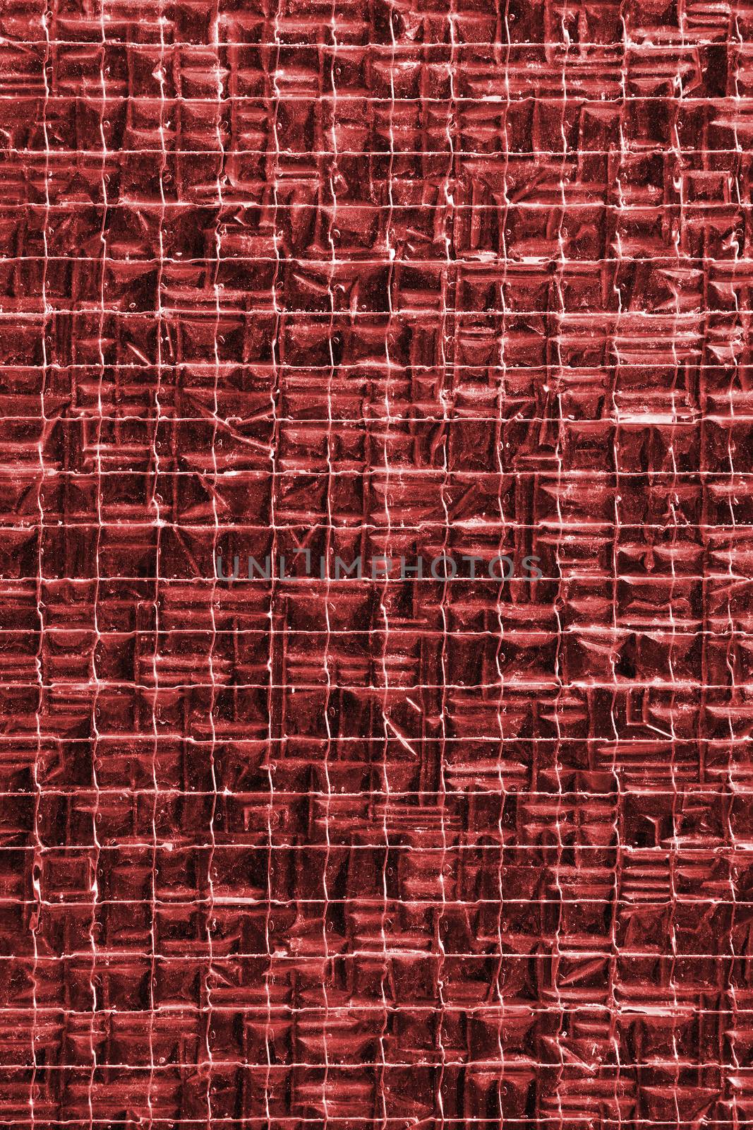 Background texture of red stained glass reinforced with metal wire mesh grid, close up