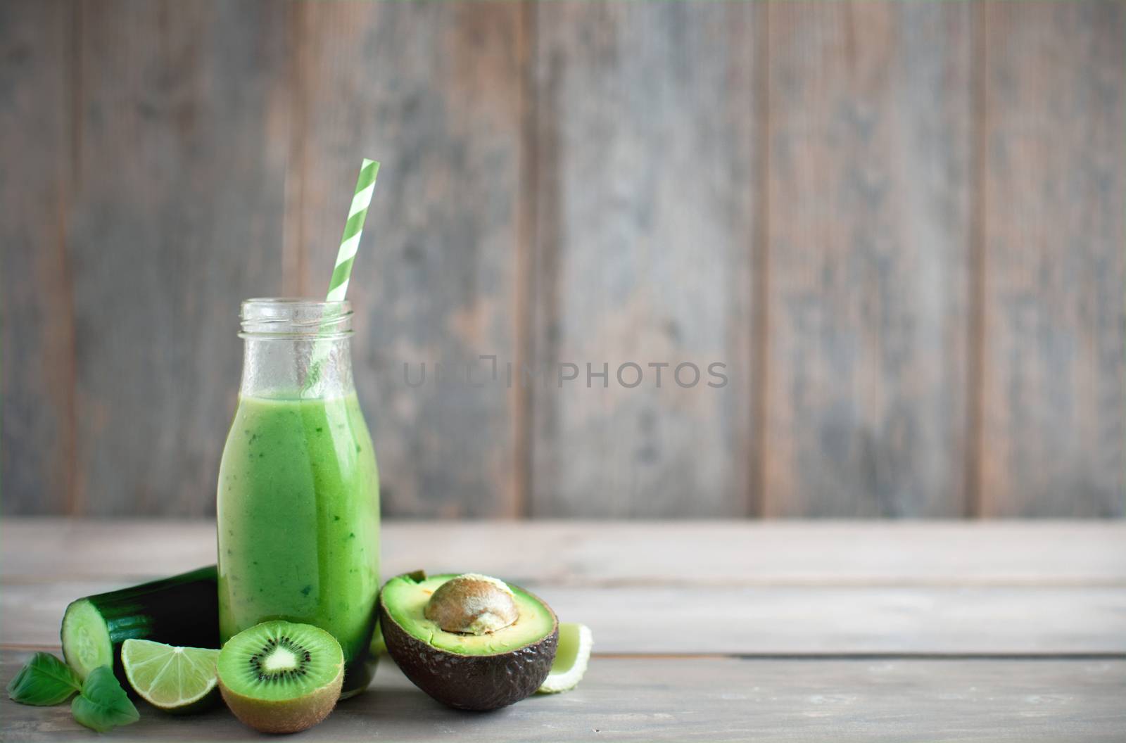 Green smoothie in a bottle with ingredients over a wooden background