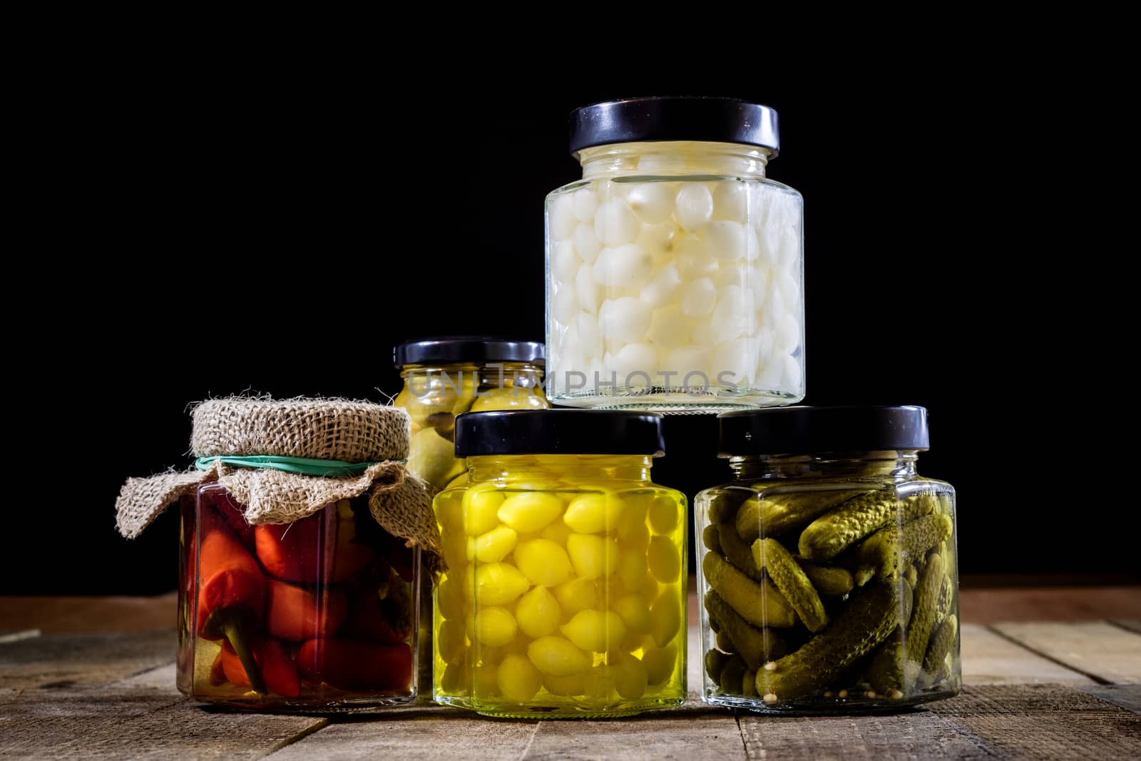 Mortar, vegetables in jars for the winter, wooden table in the old kitchen. Black background.