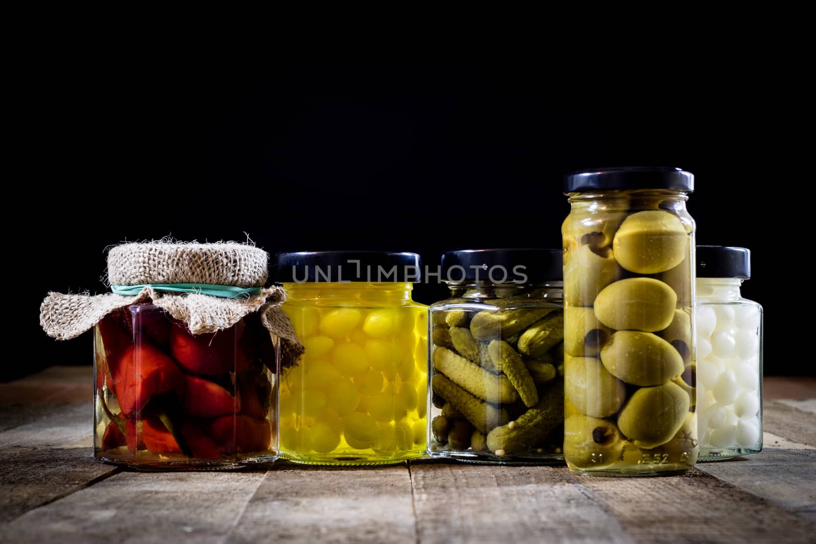 Mortar, vegetables in jars for the winter, wooden table in the old kitchen. Black background.