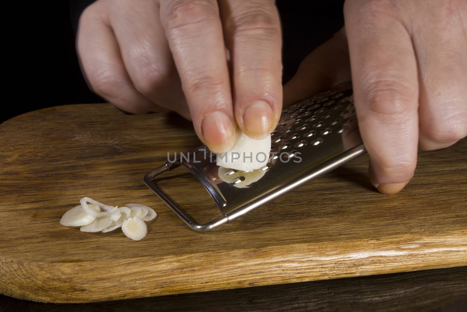 Female hands grind garlic on a grater on a black background