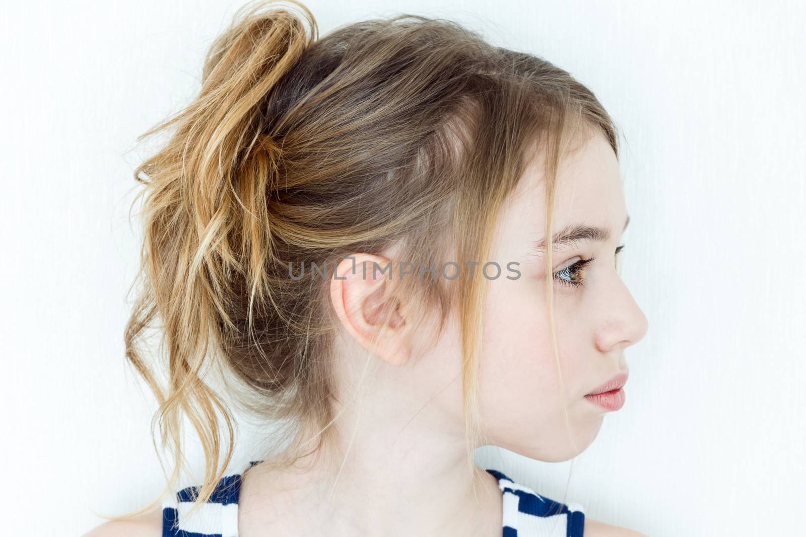 Cute girl eleven years old with blond long hair on white wall background in profile