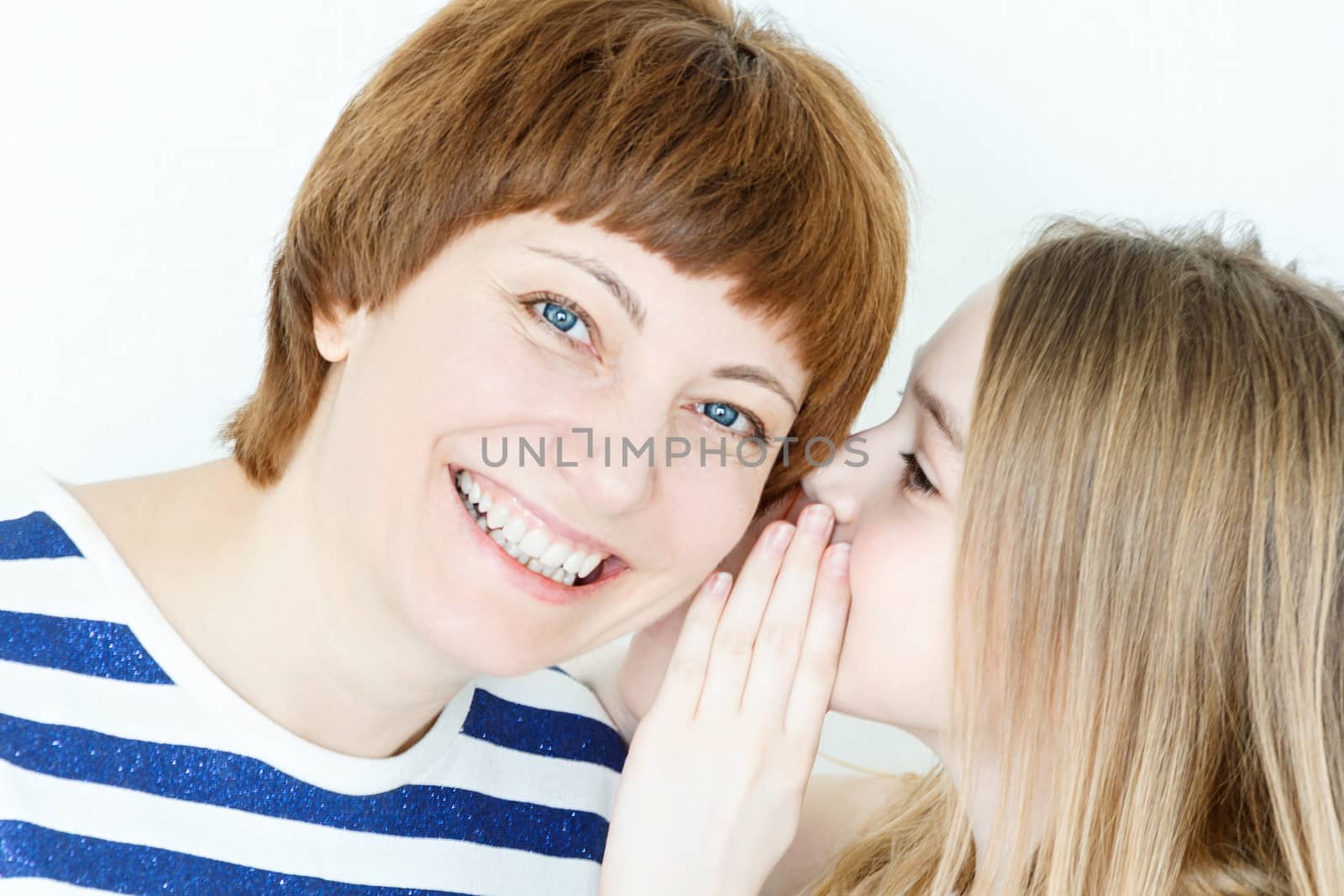 Daughter says a secret an her mother ear on white wall