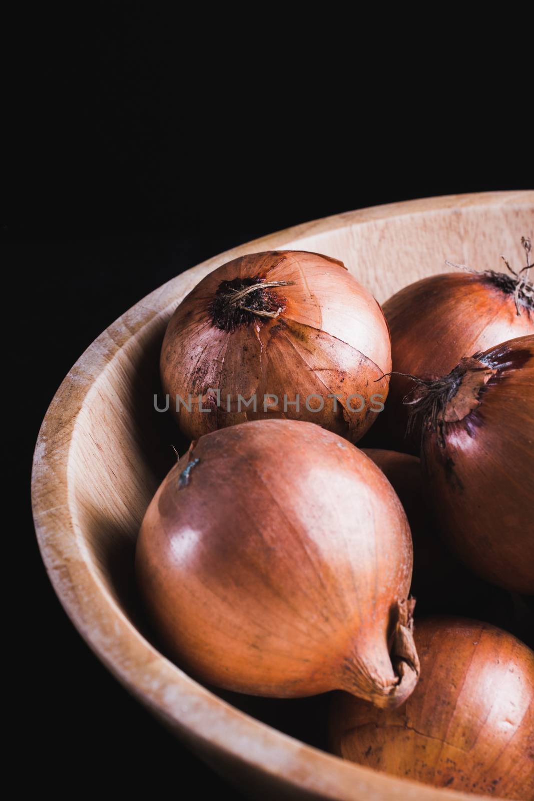 raw onions in a wooden bowl, black background
