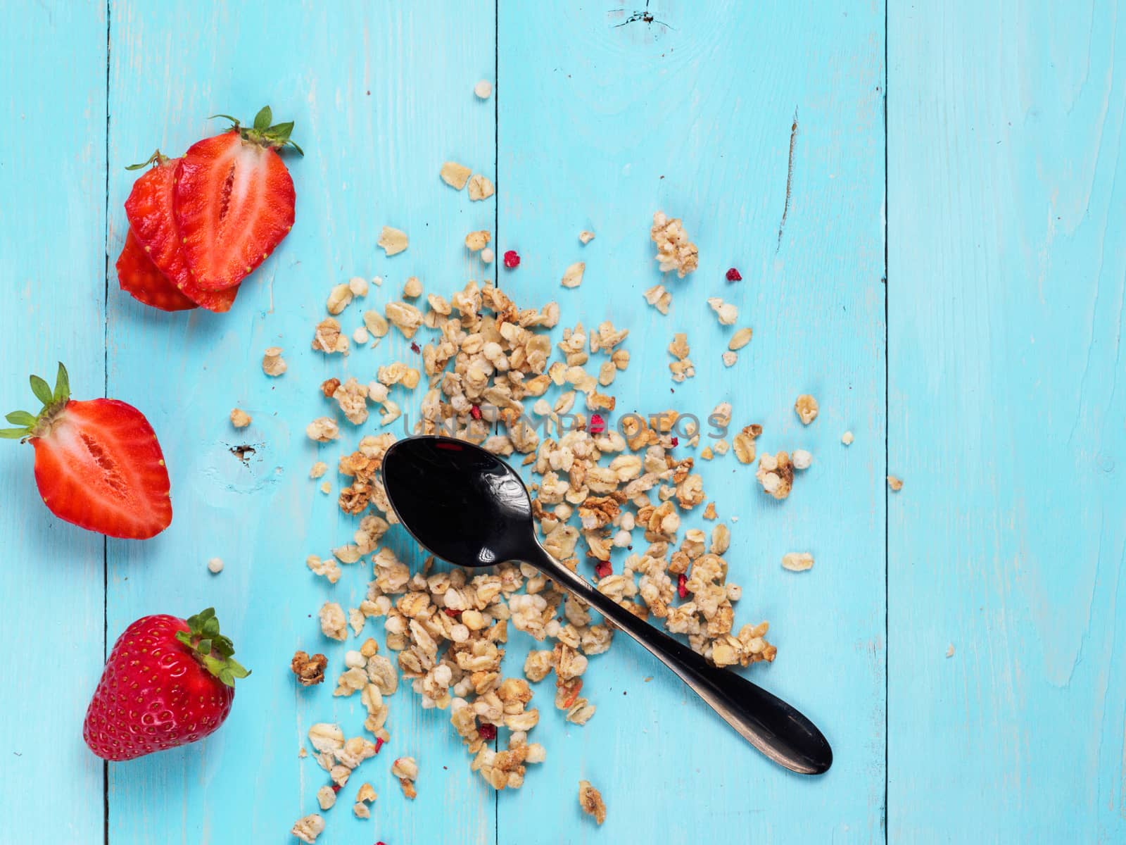 Close up view of dry muesl with black teaspoon and fresh strawberries on blue wooden background. Copy space. Top view or flat lay.