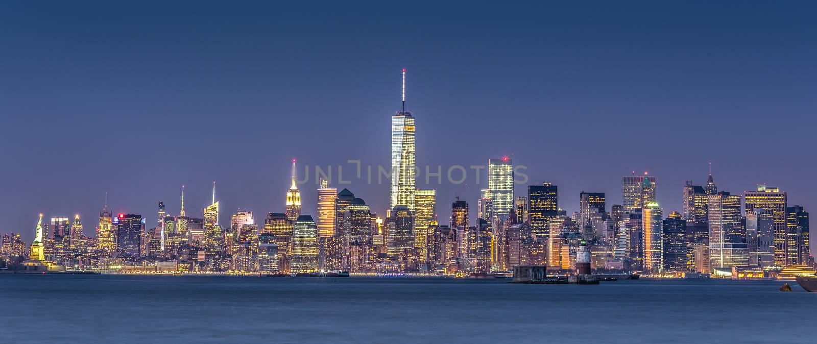 New York City Manhattan downtown skyline at dusk with skyscrapers illuminated over Hudson River panorama. Horizontal composition.