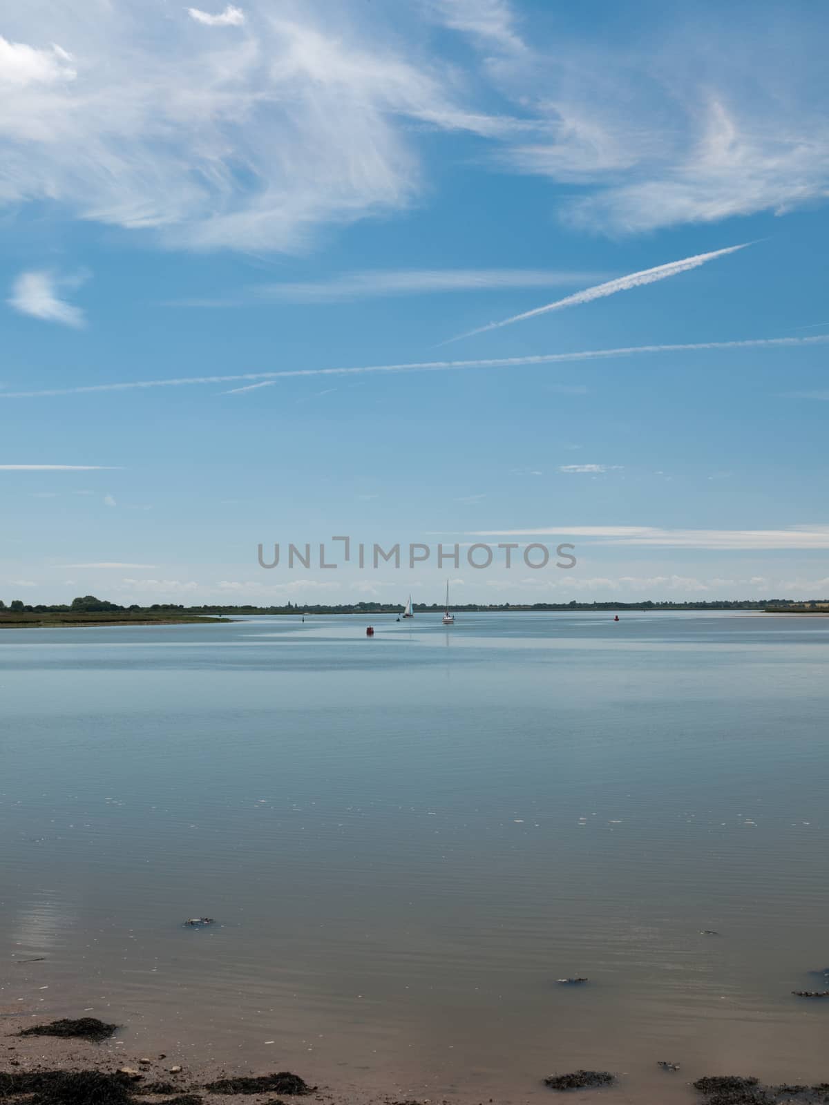 a calm and clear day on a river surface with country in the distance and buoys and boats no people beautiful