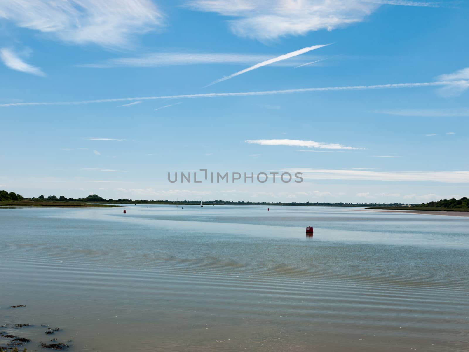 a calm and clear day on a river surface with country in the distance and buoys and boats no people beautiful