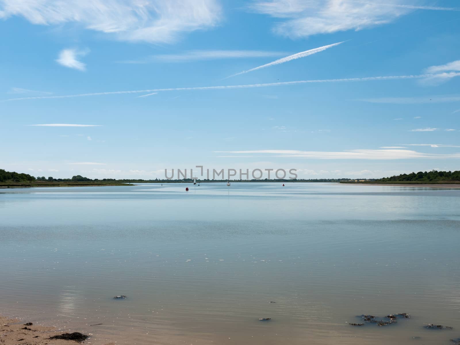 a calm and clear day on a river surface with country in the distance and buoys and boats no people beautiful