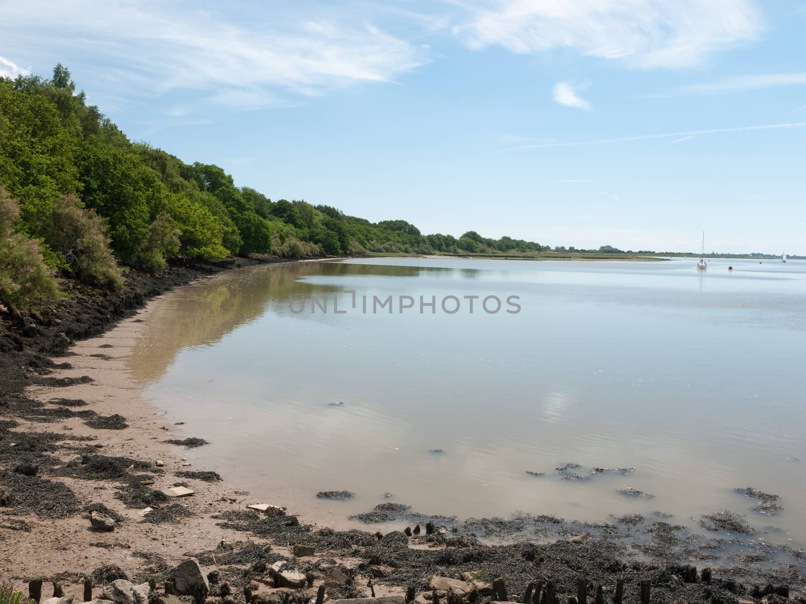 a calm and clear day on a river surface with country in the distance and buoys and boats no people beautiful and a bay with sand and rocks