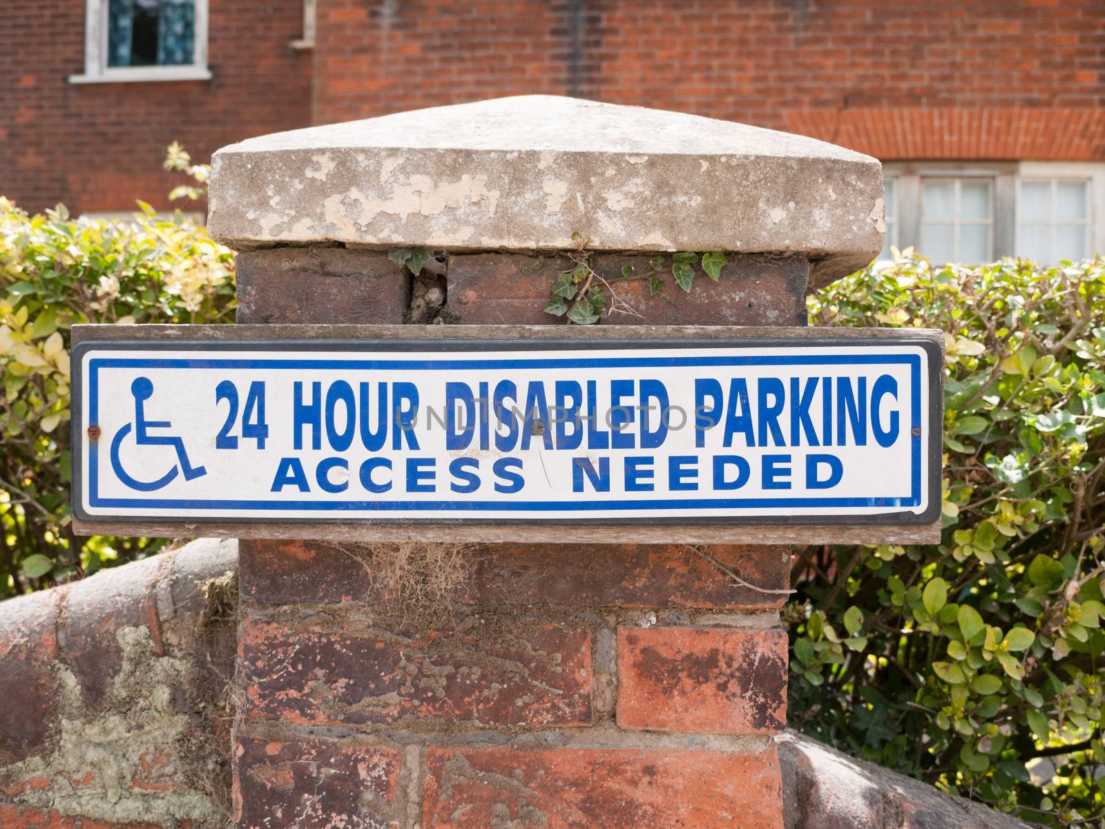 blue and white 24 hour disabled parking access sign on brick post outside