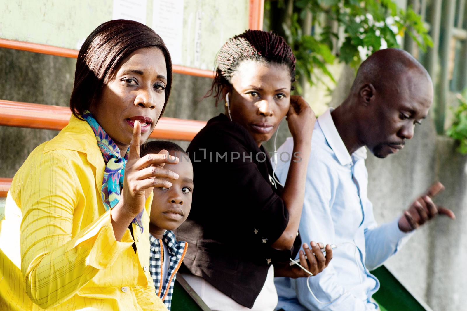 This group of people sitting at the bus stop awaits the arrival of the next bus.