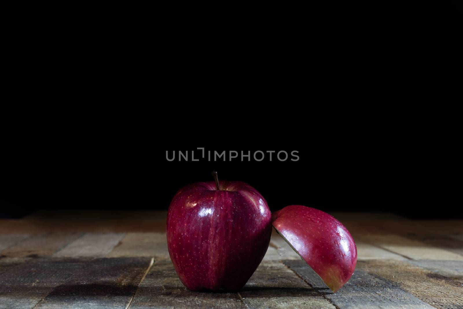 Red tasty wet apple on a wooden table. Black background.