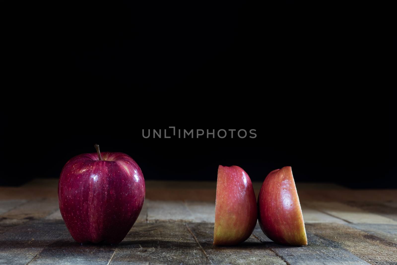 Red tasty wet apple on a wooden table. Black background.