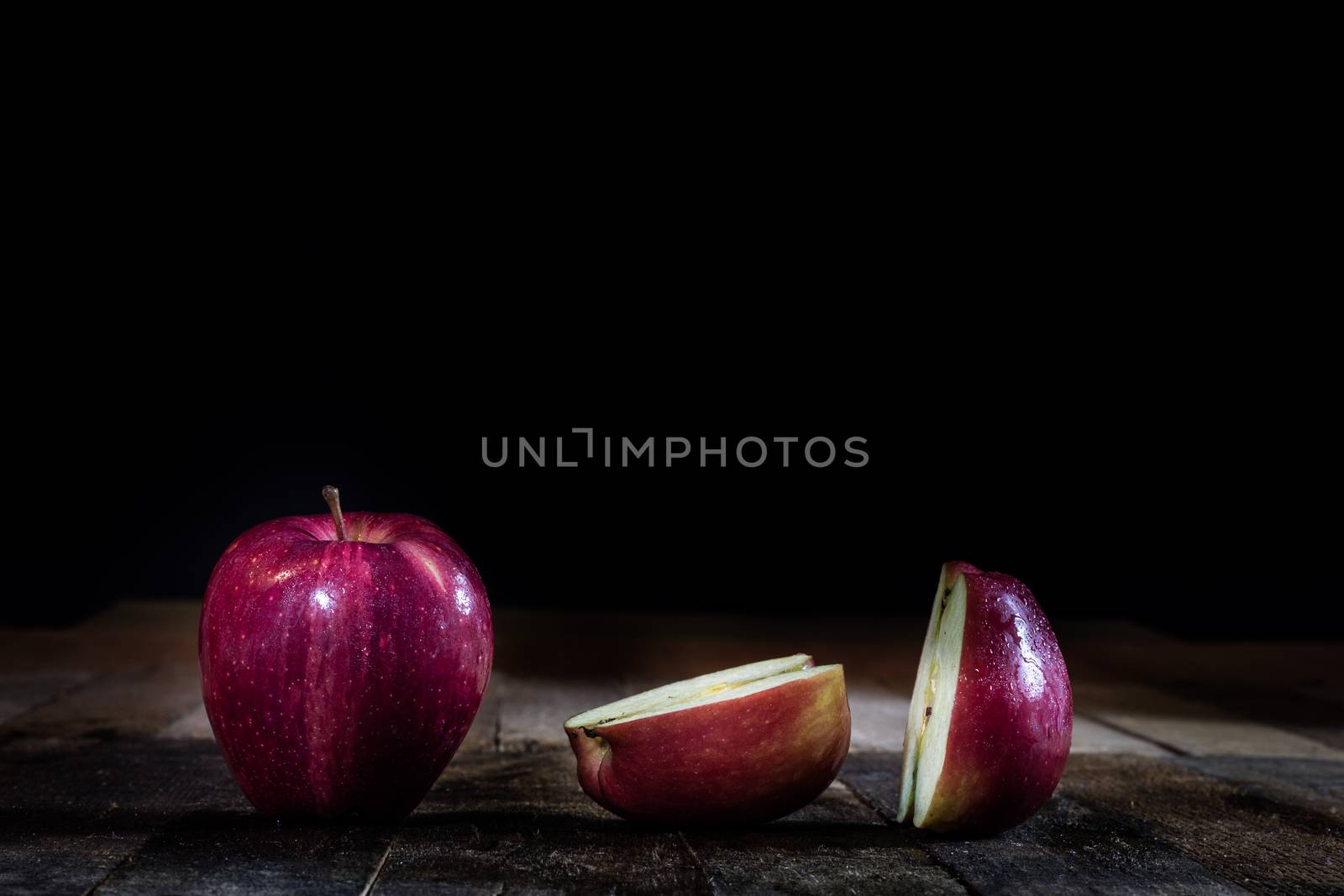 Red tasty wet apple on a wooden table. Black background.