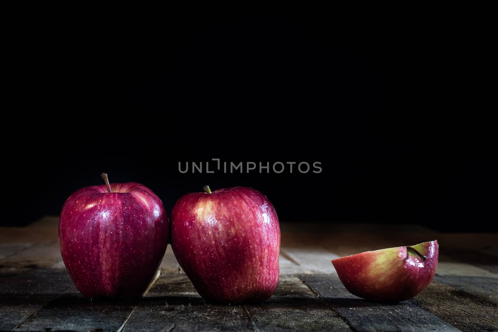 Red tasty wet apple on a wooden table. Black background.