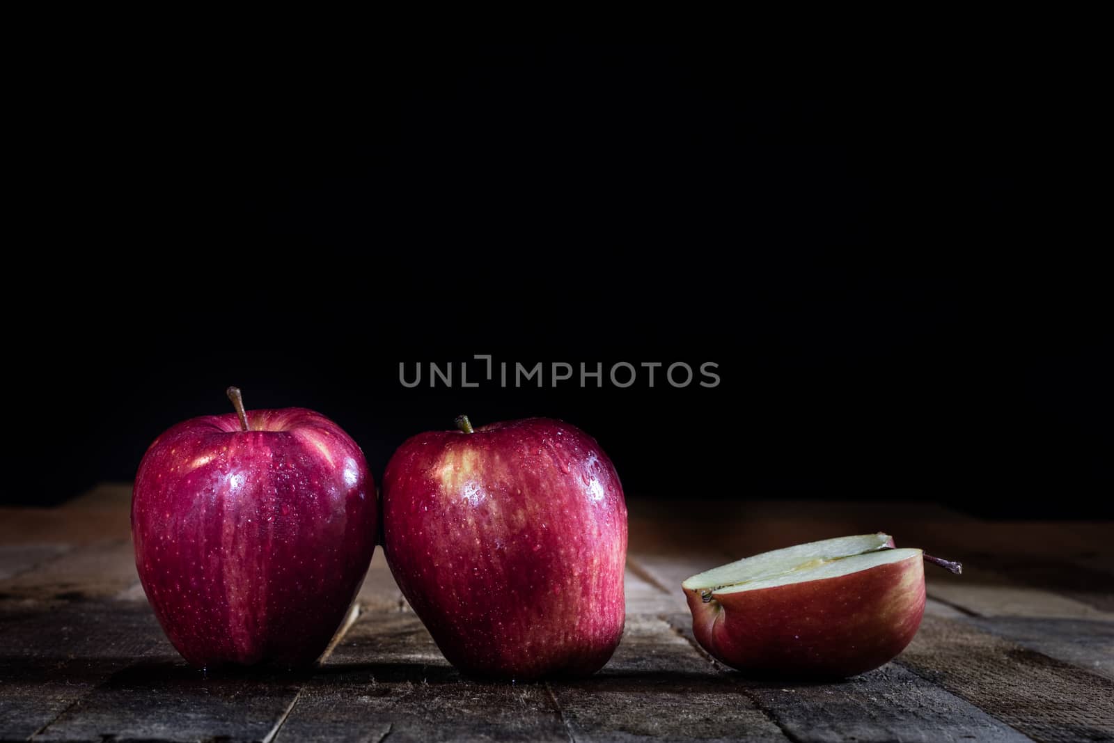 Red tasty wet apple on a wooden table. Black background.