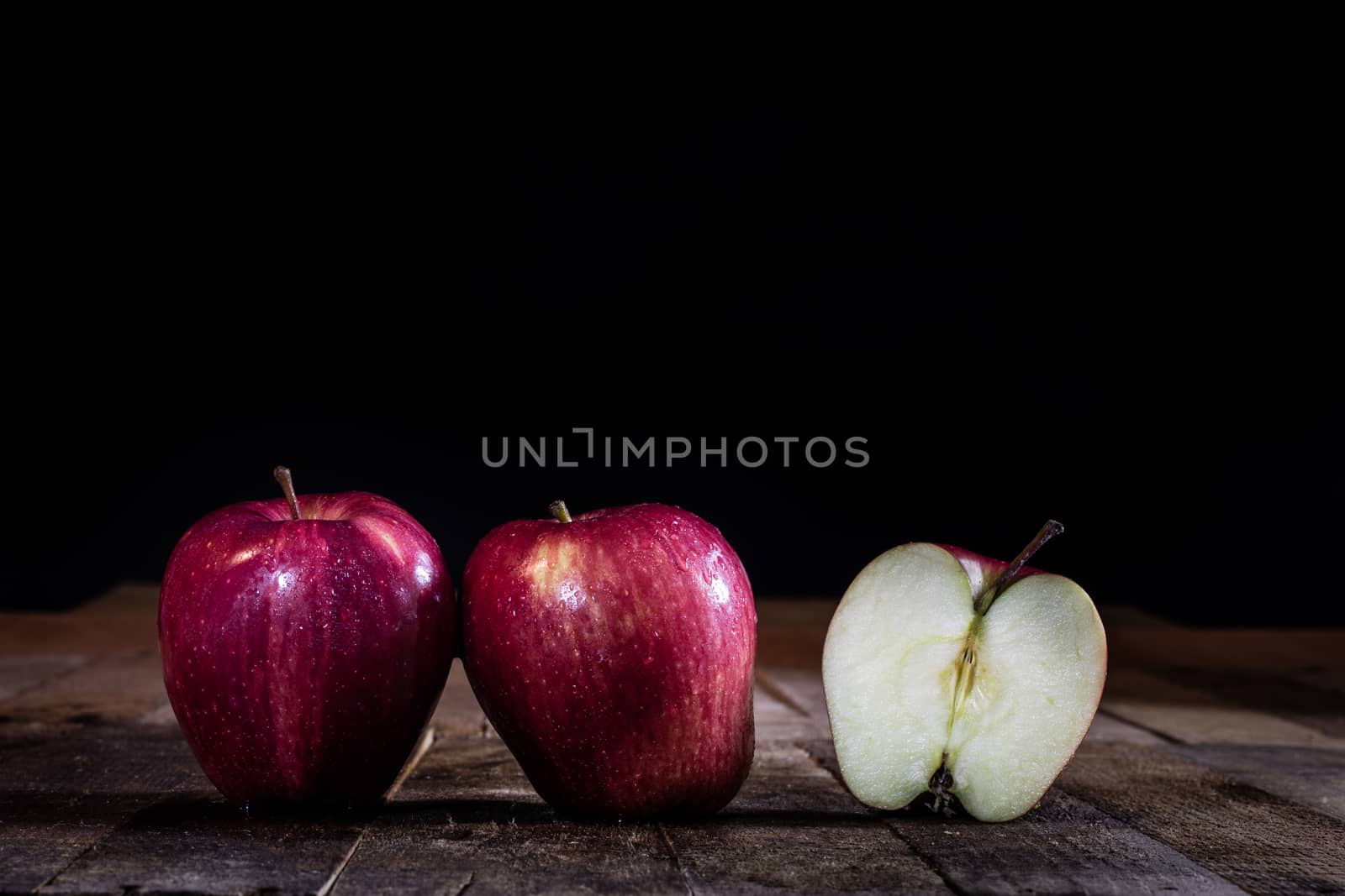 Red tasty wet apple on a wooden table. Black background.